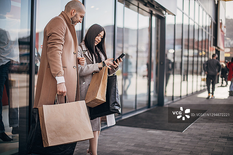 情侣在购物中心使用智能手机购物袋图片素材