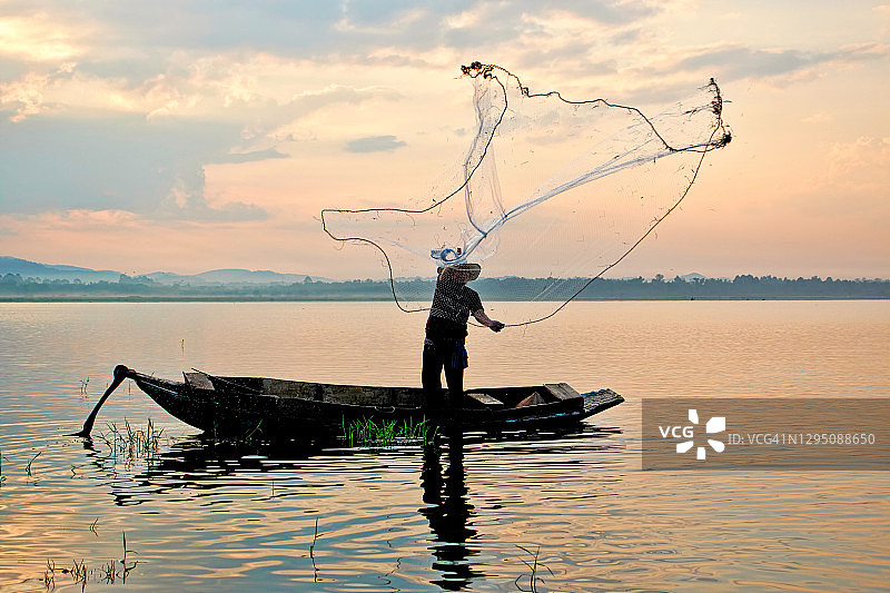 亚洲渔民在木船上，湖上有渔网图片素材