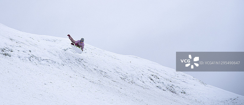 一个孩子，一个男孩，正在飞快地从一座积雪覆盖的山上滑下来。冬天好玩的周末。图片素材