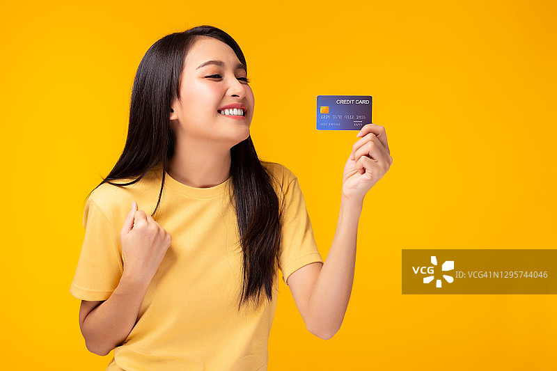 快乐的年轻亚洲妇女显示塑料信用卡和看着信用卡与快乐站在黄色的背景客户女孩得到满意的信用卡服务与微笑的脸图片素材