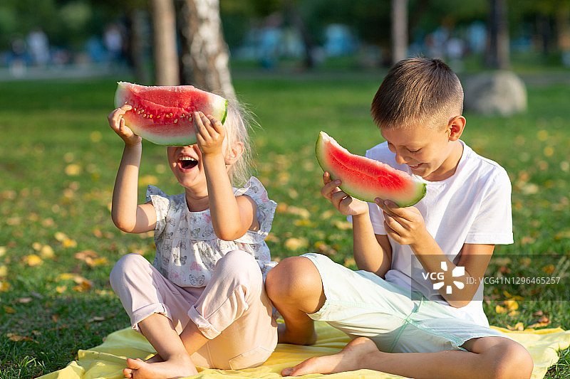 给可爱的孩子们，小男孩和小女孩在秋季公园草地上野餐，吃着多汁的西瓜图片素材