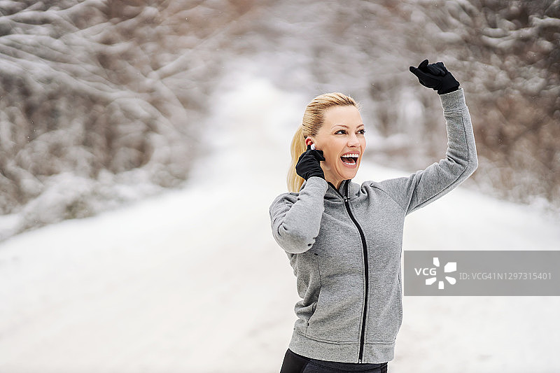 快乐的女运动员，在大雪纷飞的冬日里，一边欣赏音乐，一边在锻炼中休息。健康生活，乐趣冬季健身图片素材