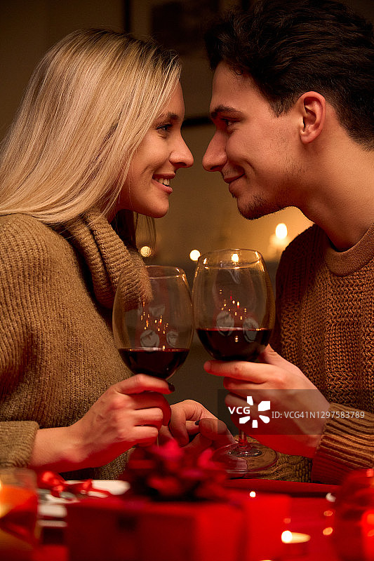 甜蜜的小情侣，手握酒杯，喝着红酒，一起享受温柔的时刻，一起庆祝情人节，烛光晚餐，坐在家里或餐厅。图片素材