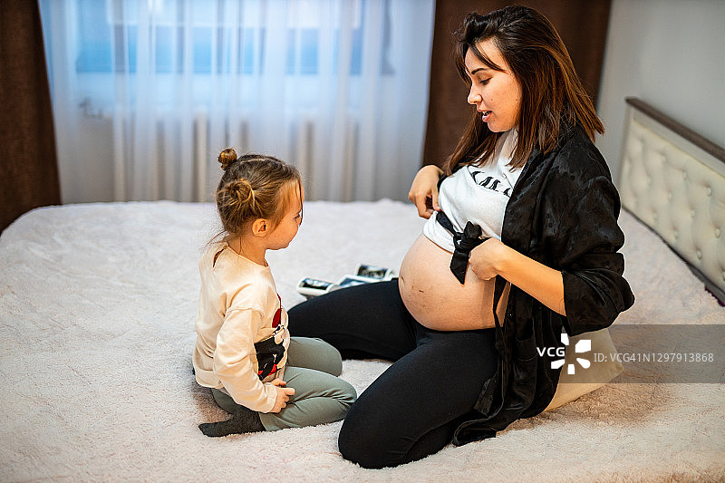 孕妇向蹒跚学步的女儿展示肚子图片素材