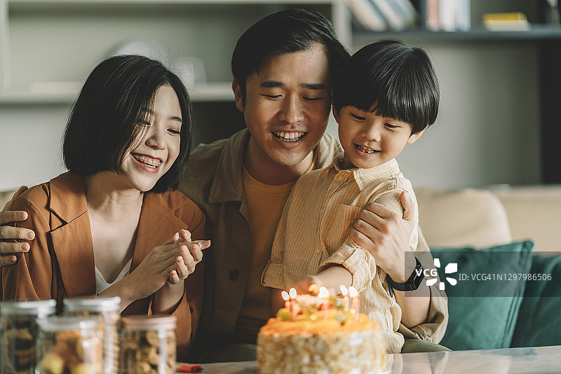 可爱的亚洲中国男孩和他的父母在他的生日蛋糕上点燃蜡烛图片素材