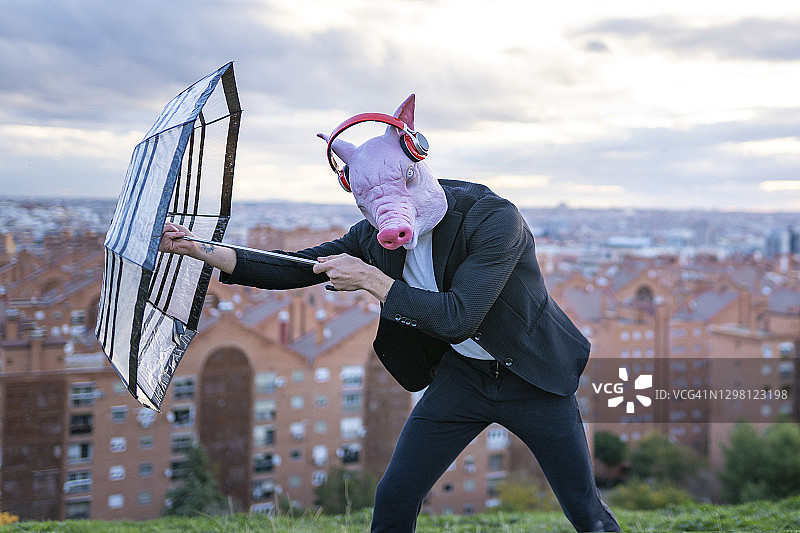 男企业家戴着猪面具和无线耳机与雨伞奋力对抗天空图片素材