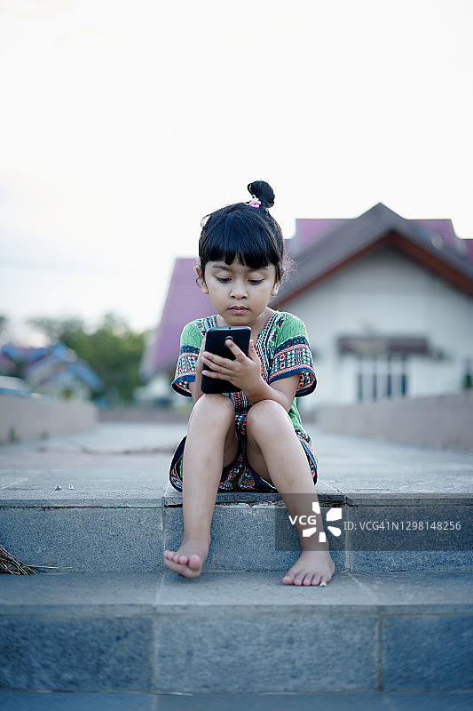 可爱的小女孩在公园里玩智能手机图片素材
