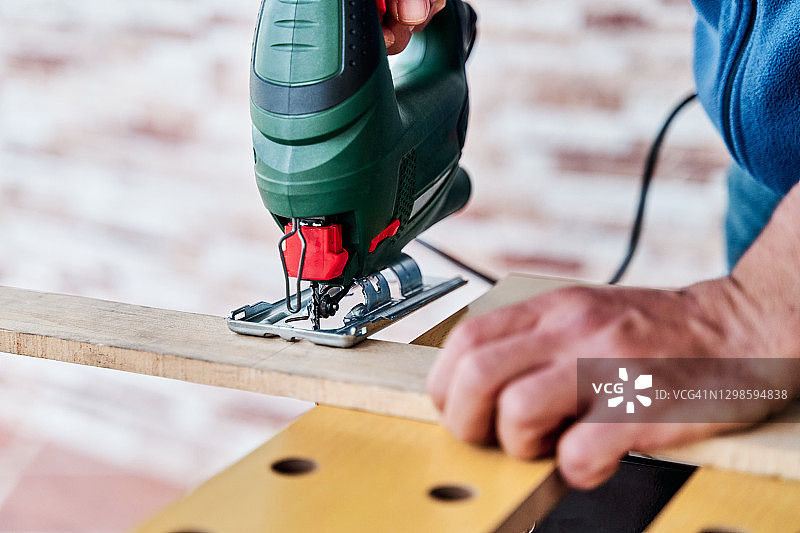 一个不认识的人用夹具锯切割一块木头的细节视图。diy的概念，木工和木工在家里。图片素材