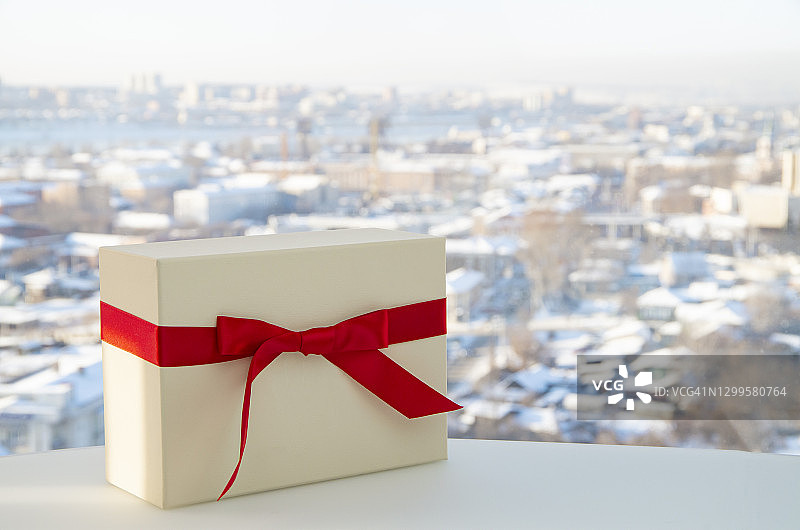 以城市为背景，用红丝带系上白色礼盒。水平构图与复制空间。非常适合圣诞节和情人节的礼物。图片素材