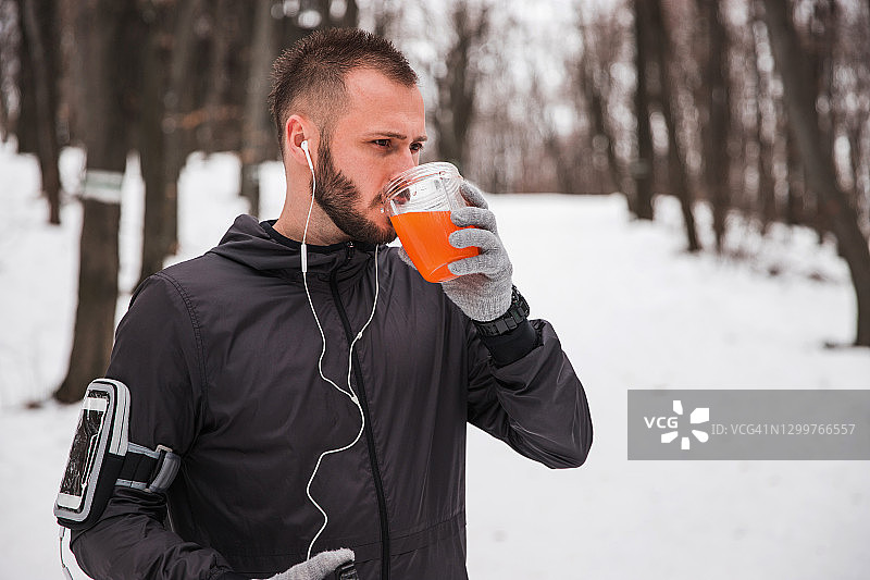 在雪地上跑步后喝橙汁的男人图片素材