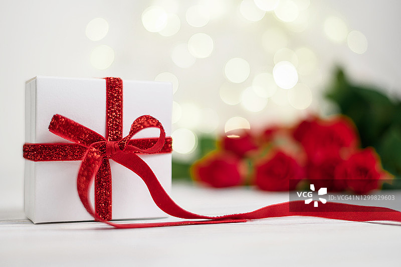 白色礼盒，红色蝴蝶结，背景红玫瑰和散焦，祝贺圣瓦伦丁节，母亲节。图片素材