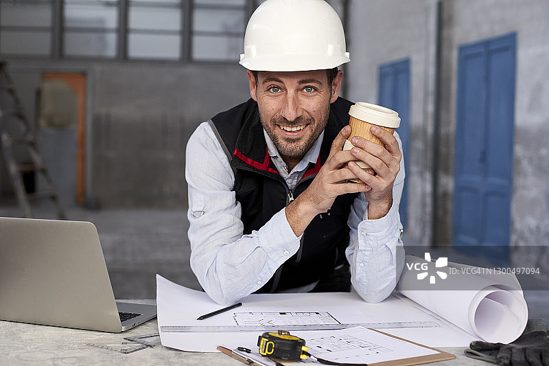 微笑的男建筑师拿着咖啡杯站在大楼的桌子旁图片素材