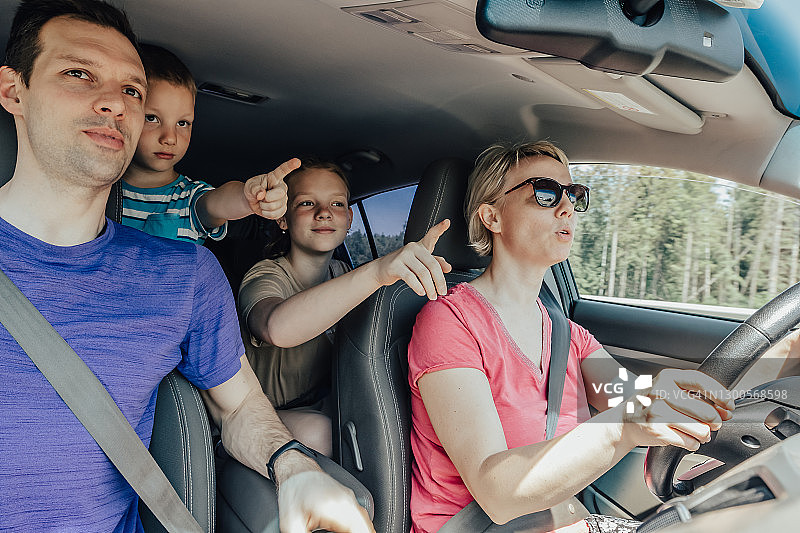 在父母开车的公路旅行中没有系安全带的孩子。一家人在车里一起向前看图片素材