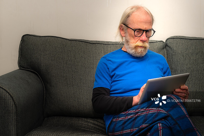 一位退休男子在家里的沙发上休息，同时使用着数字平板电脑图片素材