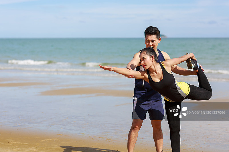一对亚洲夫妇锻炼前在海滩上做伸展运动。年轻的男人和女人在夏季锻炼。图片素材