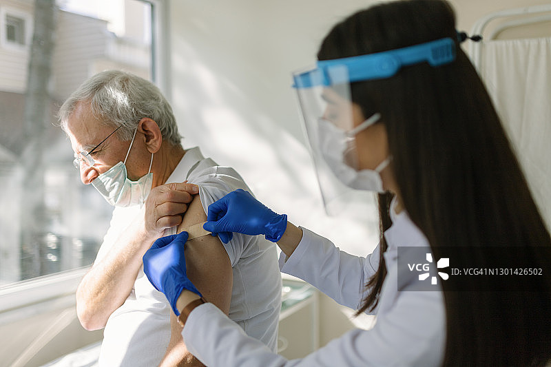女医生穿着防护服在老年病人的手臂上注射疫苗图片素材