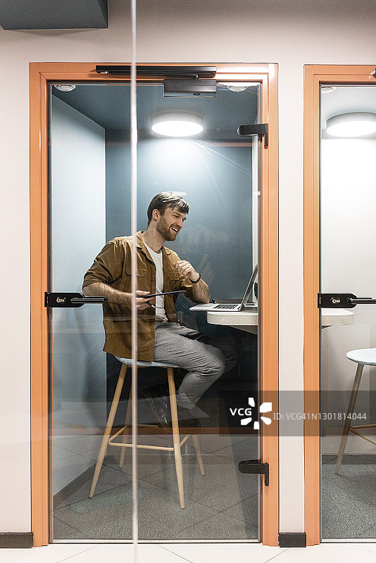 透过办公室的玻璃门可以看到通过笔记本电脑进行视频通话的男性职业人士图片素材