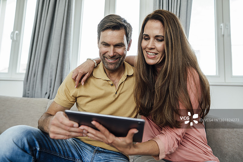 微笑的成熟夫妇在家里的沙发上使用数码平板电脑图片素材
