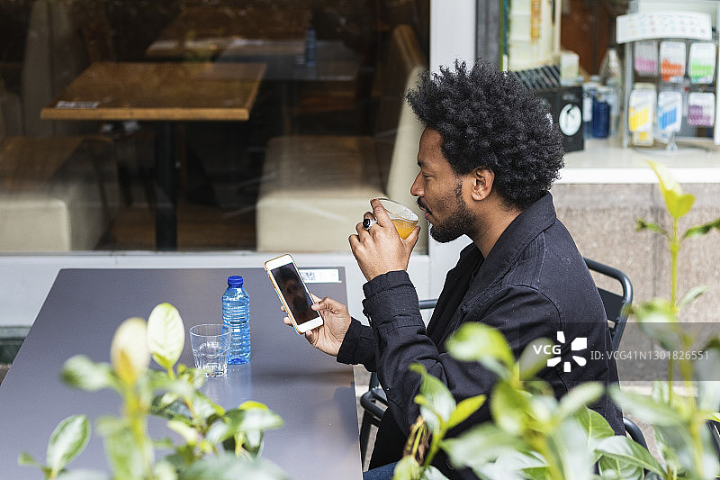 一个留着非洲发式的男人在路边咖啡馆边喝边用手机图片素材