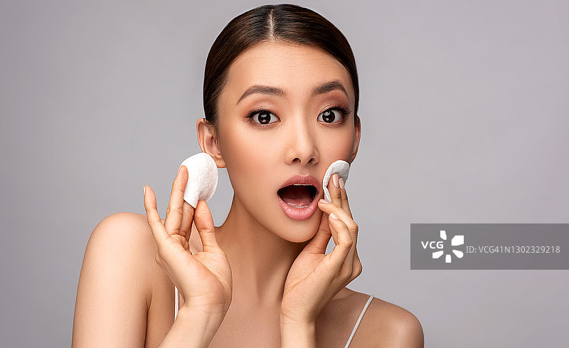 中国美女模特正在用棉垫触摸脸颊的皮肤。皮肤护理和化妆品。亚洲的美丽。图片素材