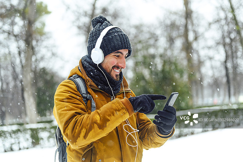 冬天，一名男子在雪地上一边用手机一边戴着耳机听音乐图片素材