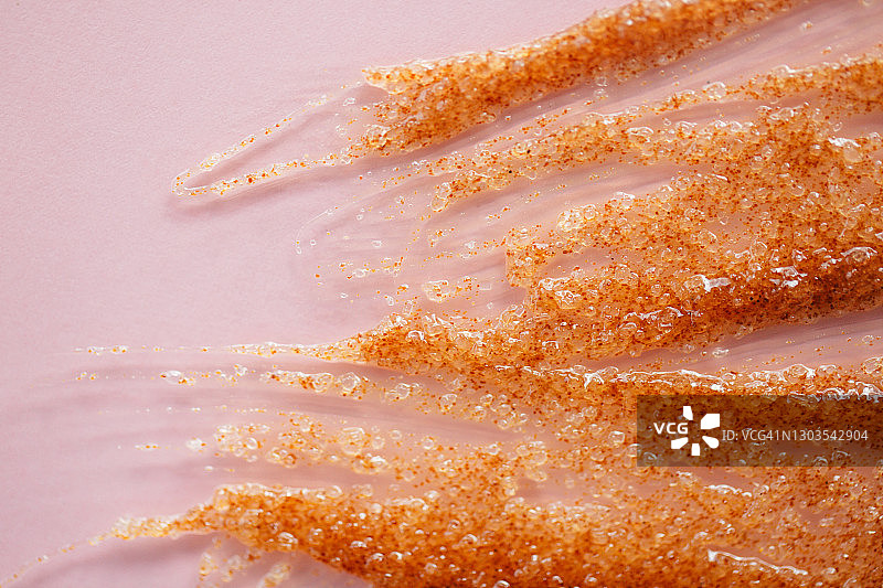 橙色磨砂膏的纹理与去角质颗粒在玫瑰背景。自我护理是今年流行的方法。化妆品广告图片素材