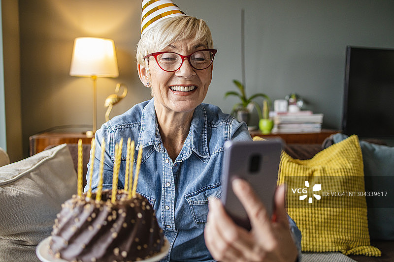 一位年长的女士正拿着一个生日蛋糕，通过手机进行视频通话图片素材