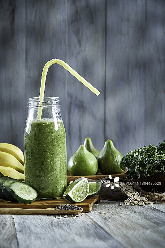 健康食品:瓶子里的绿色排毒奶昔放在质朴的桌子上。图片素材