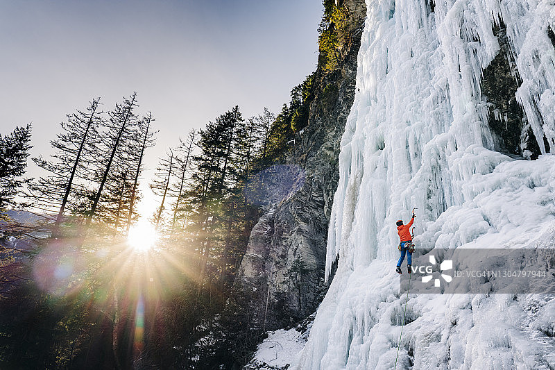 一个冰上攀登者攀登一个高高的冰冻瀑布，就像在一个戏剧性的日出图片素材