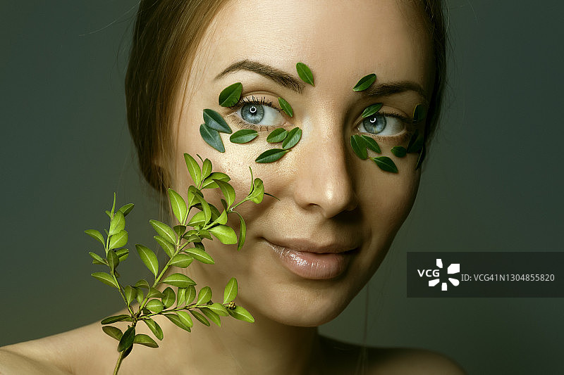 年轻女子肖像与自然化妆模糊与散焦黄杨木枝。绿叶贴在脸上。草药的概念。图片素材
