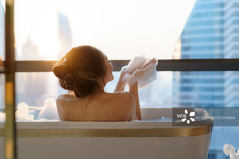 一名亚洲女子度假时在市中心豪华酒店浴室的浴缸里用肥皂泡洗澡。图片素材