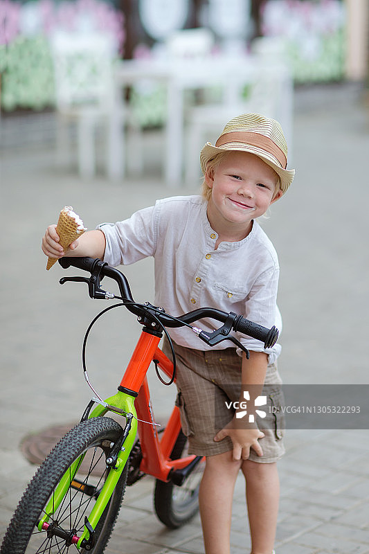 一个骑着自行车的金发男孩试着拍他的冰淇淋库存照片。图片素材