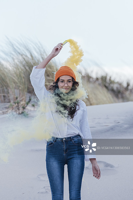 年轻女子在橙色编织头发与遇险火炬站在天空在海滩图片素材