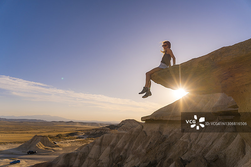生活方式会议的一个年轻的金发女郎在沙漠的石头在一个日落在巴尔德纳斯里尔斯，西班牙图片素材
