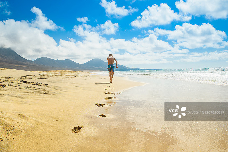 在假期，男孩在海边跑步在夏天。Cofete海滩图片素材