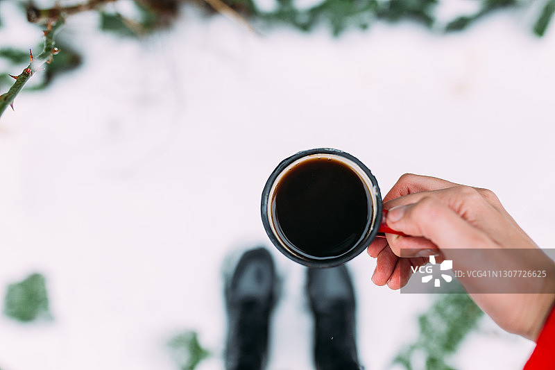 在雪中，手拿着红搪瓷杯，盛着热咖啡图片素材