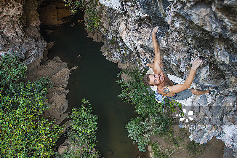在老挝，一名男子正在攀爬悬在悬崖上的石灰岩图片素材