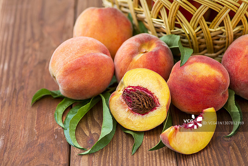 新鲜多汁的桃子和叶子在柳条篮子里，在一个木制的背景。柳条篮子里刚摘的桃子。图片素材