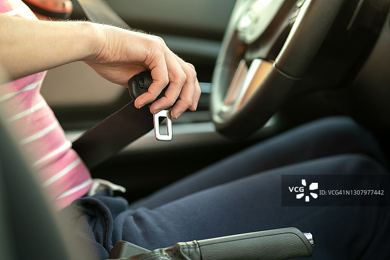 近女子手系安全带，而坐在车内安全驾驶前的道路上。女司机开车安全，旅途安全。图片素材