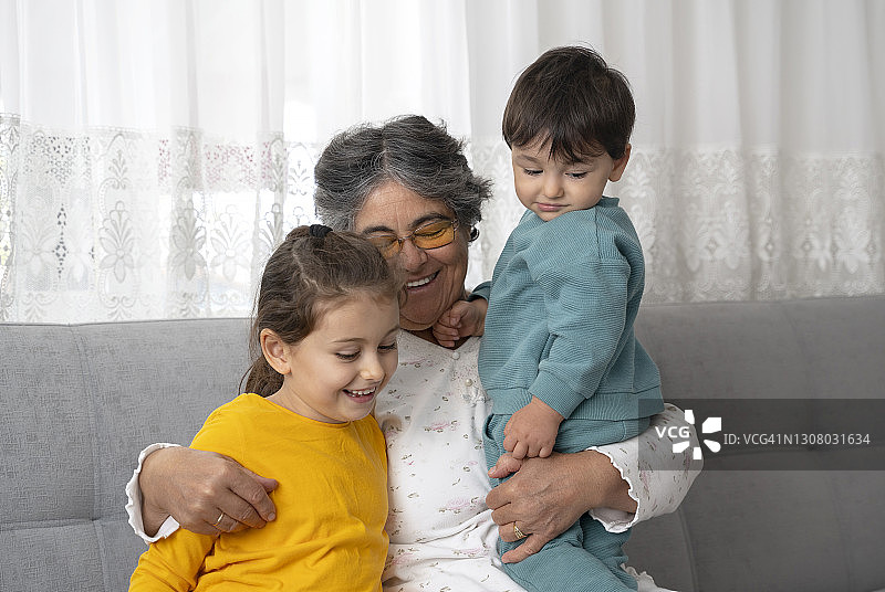 快乐的老祖母坐在客厅的沙发上拥抱着孙女，还有孙子图片素材