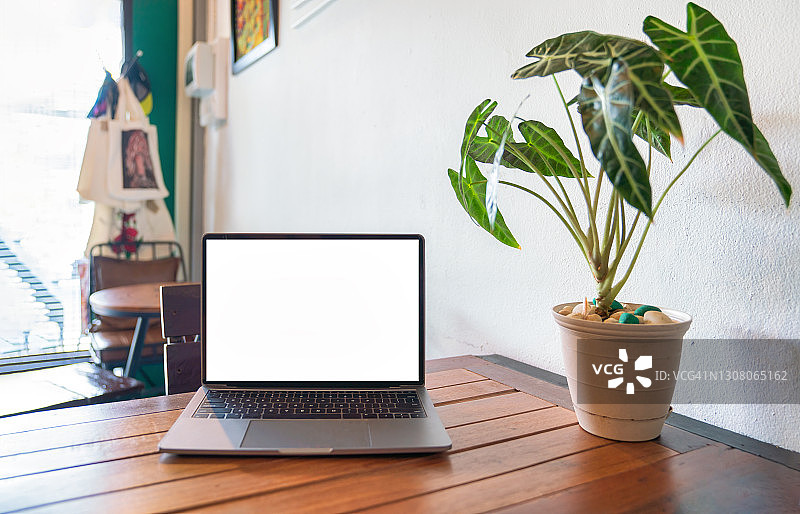 笔记本电脑空白屏幕上的桌子在咖啡馆的背景。笔记本电脑与空白屏幕上的咖啡店模糊背景。- - -库存图片图片素材
