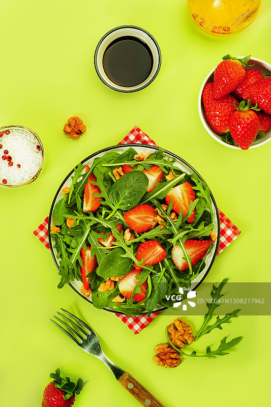夏季草莓沙拉，以菠菜叶，芝麻菜，核桃，香醋和橄榄油调味，鳄梨绿为背景。健康食品的概念。俯视图，复制空间图片素材