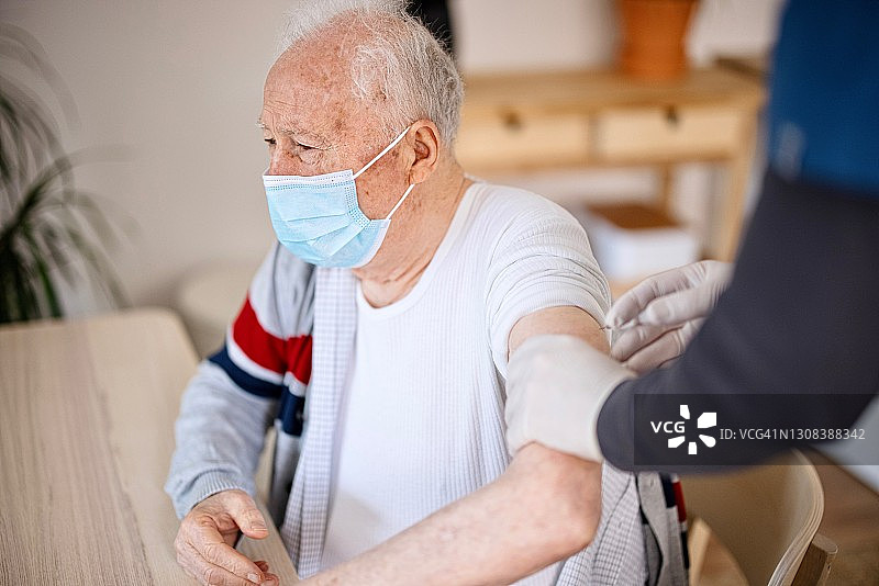 老人戴着防护口罩在家接种疫苗图片素材