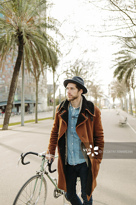 潮人戴着帽子和自行车站在城市，而看向别处图片素材