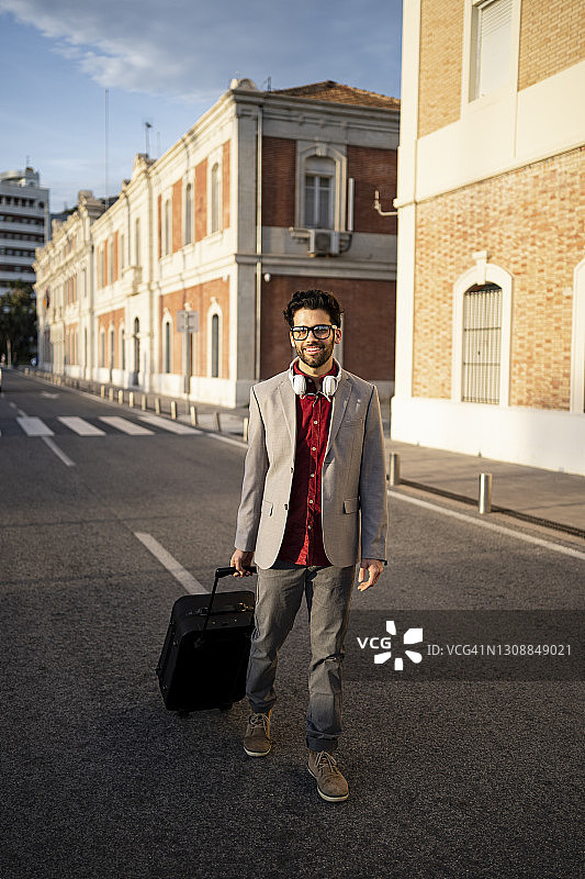 微笑的男企业家提着行李箱走在路上图片素材