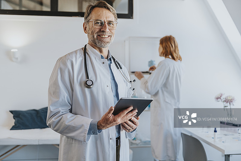 微笑的医生与同事站在数字平板电脑在诊所的背景图片素材