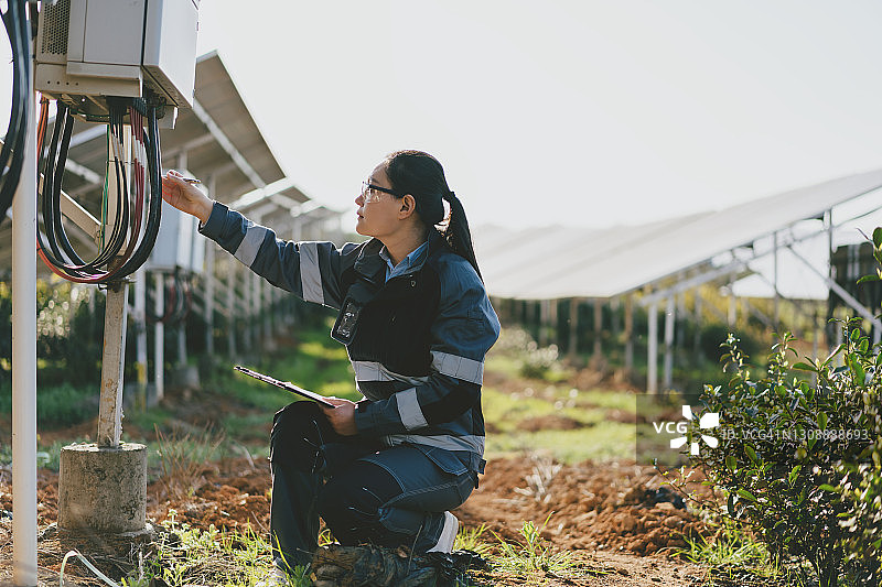 亚洲女工程师与笔记本电脑工作在太阳能发电站在日落图片素材