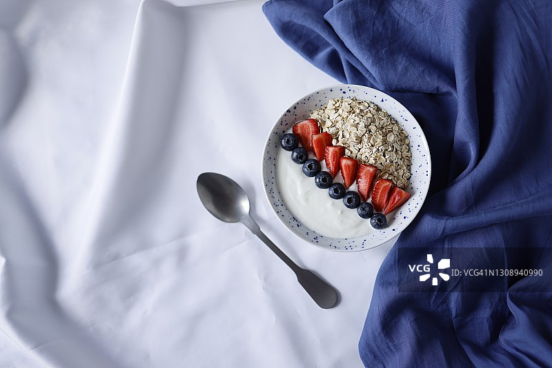 一碗健康早餐，用燕麦酸奶装饰草莓和蓝莓，盘子旁边是一个哑光金属勺和蓝色餐巾，社交媒体趋势早餐图片素材