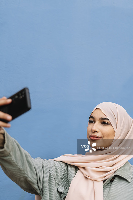 阿拉伯妇女微笑着在户外用手机自拍。图片素材