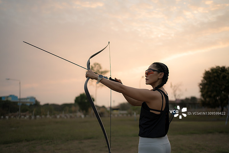 女运动员在日落时在运动场上射箭的后视图。图片素材